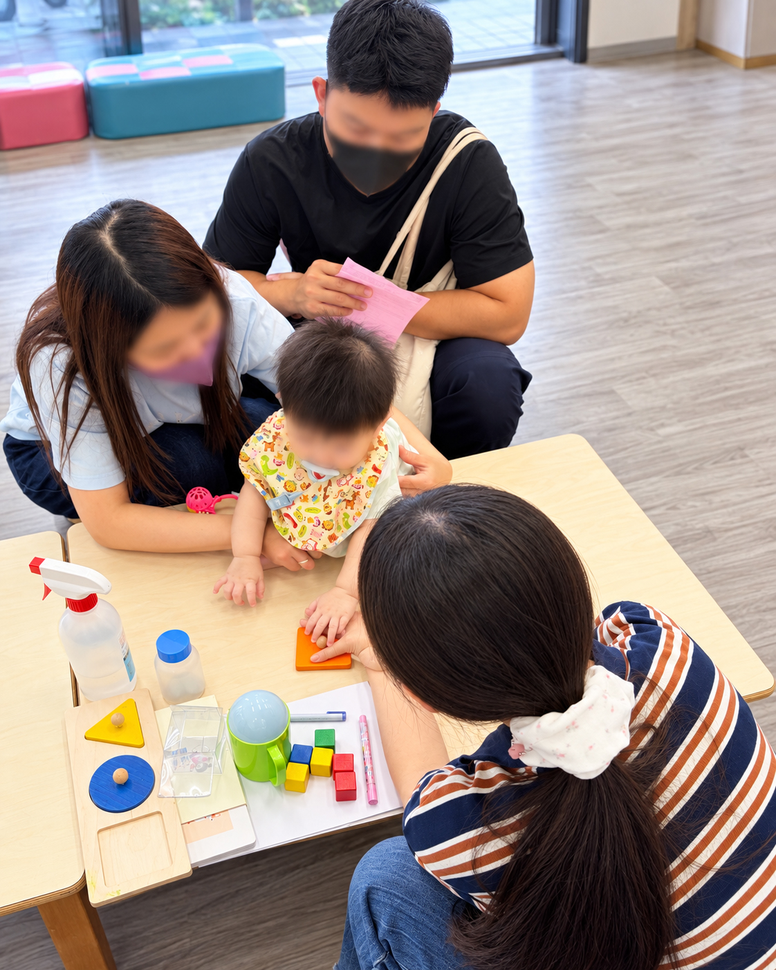 家長陪伴幼兒在桌邊操作形狀板，工作人員在旁引導