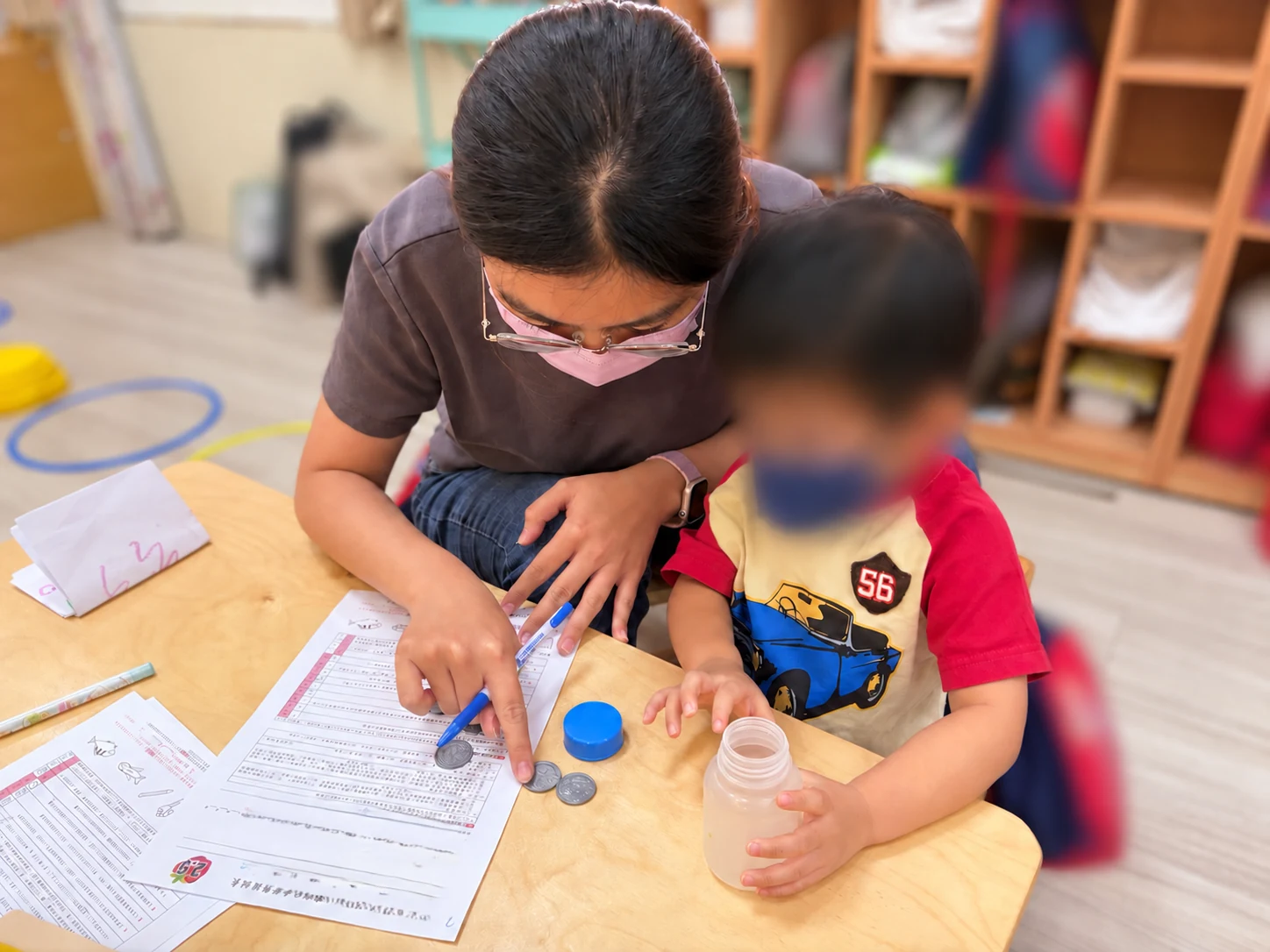 工作人員坐在幼兒身旁，陪孩子在桌邊操作瓶子與材料