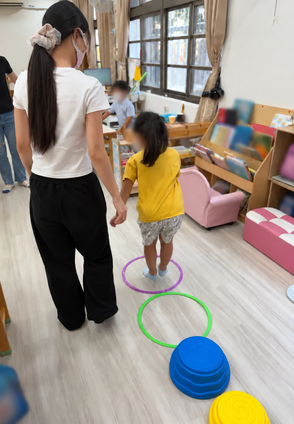 老師牽著幼兒，在教室裡沿著地上的圈圈進行動作活動