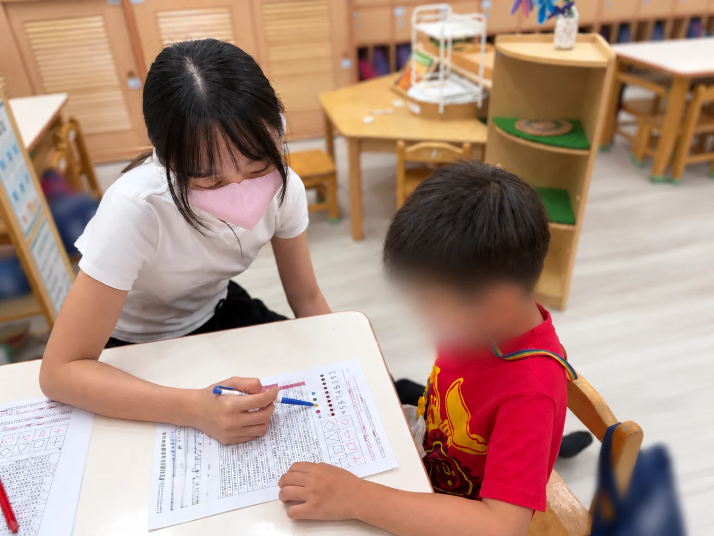 工作人員拿筆指向紙上的圖案，陪幼兒觀看與指認
