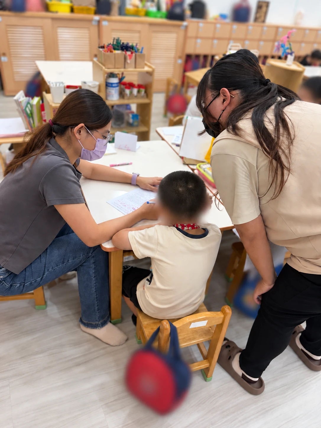 成人靠近桌邊，陪幼兒和工作人員進行紙本互動