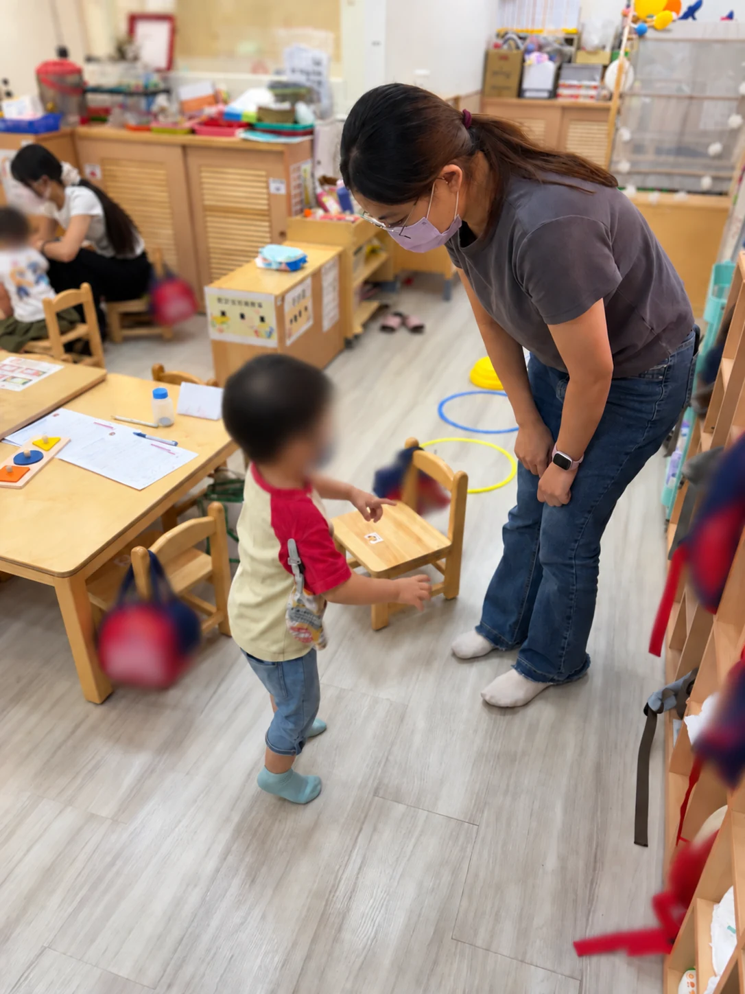 工作人員彎下身與站在教室裡的幼兒互動